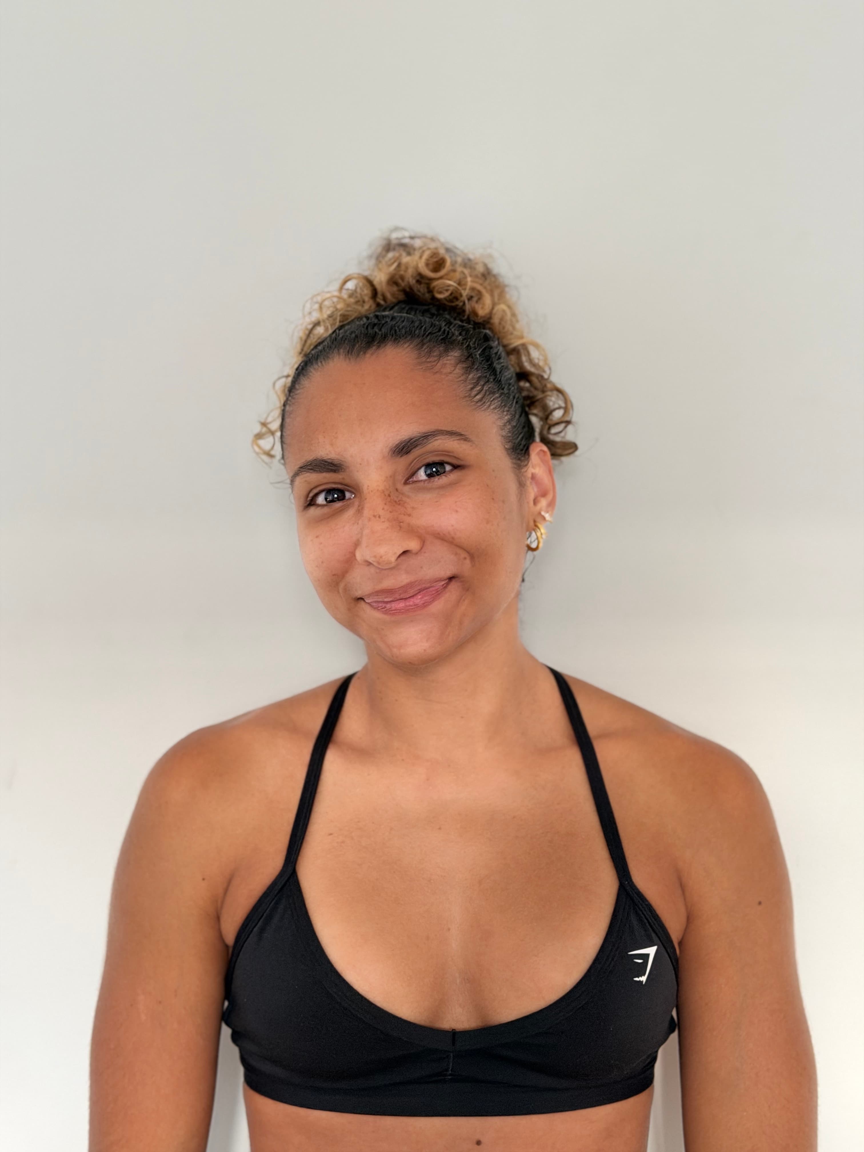 Portrait d’Andrea, coach sportive, souriante devant un mur clair.